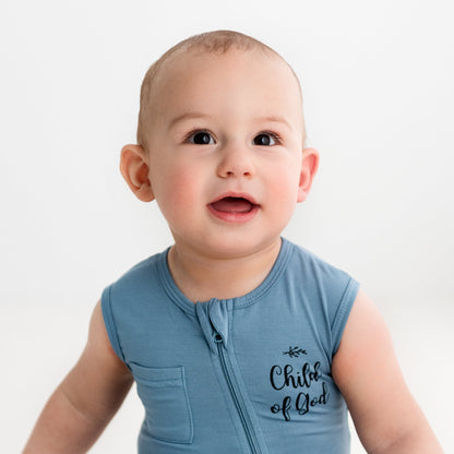 A close-up of a baby smiling while wearing the Apostle Living Inc. blue "Child of God" romper with a zipper and chest pocket.