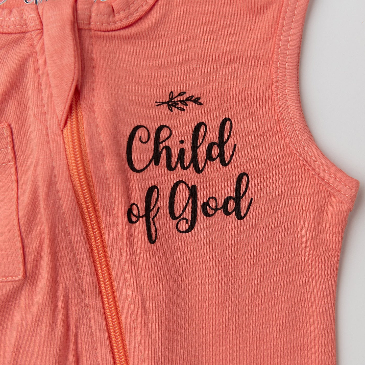 A close-up detail shot of the chest on the Apostle Living Inc. pink romper, highlighting the black "Child of God" script and the orange zipper.