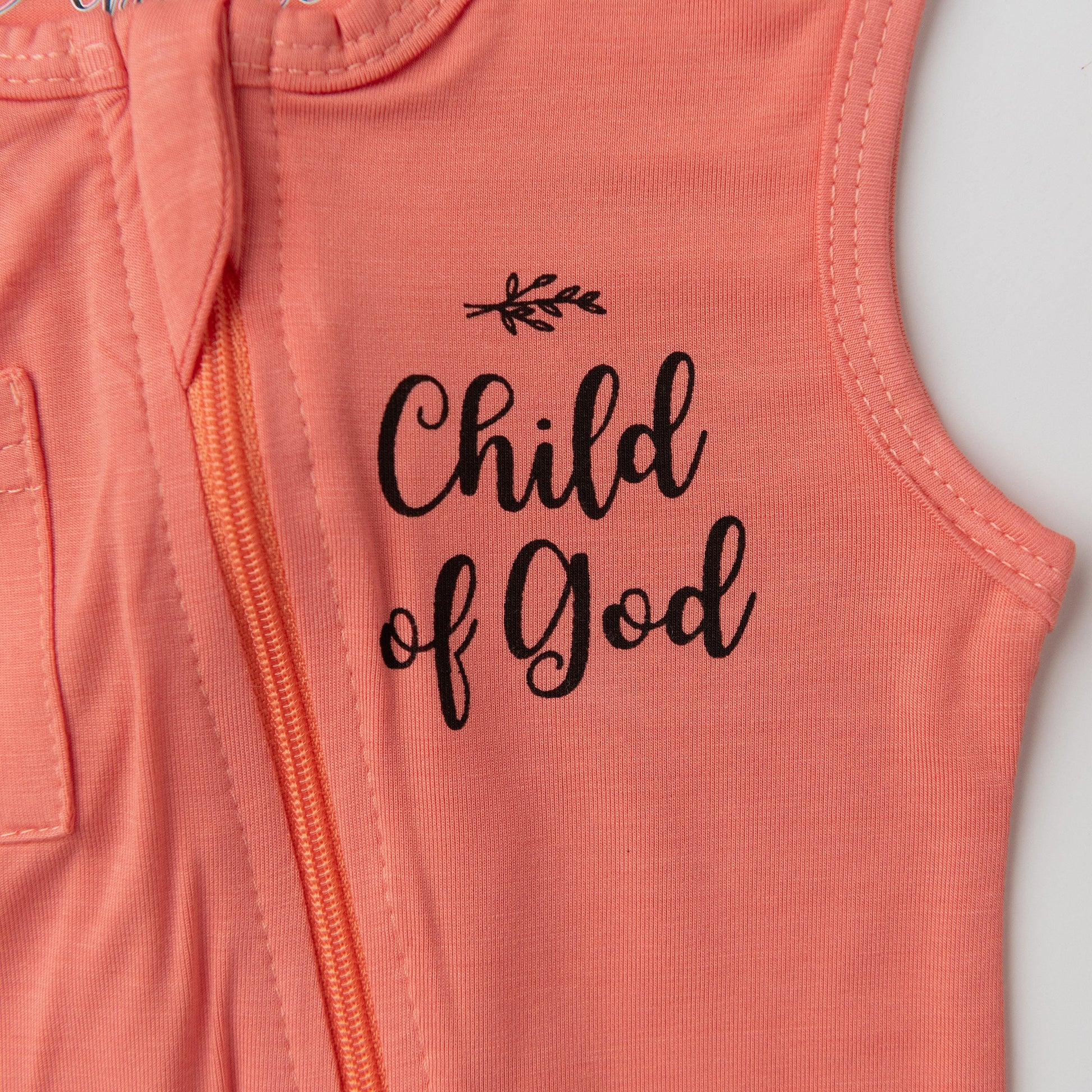 A close-up detail shot of the chest on the Apostle Living Inc. pink romper, highlighting the black "Child of God" script and the orange zipper.