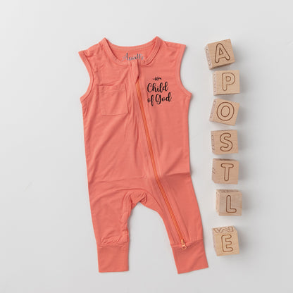 The Apostle Living Inc. pink "Child of God" romper with a zipper, styled in a flat lay with wooden blocks that spell out the brand name Apostle.