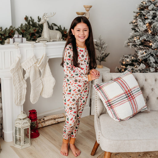 A young girl with Apostle Living smiling and posing in a soft ivory-colored bamboo Christmas pajama set with a festive holiday print.


