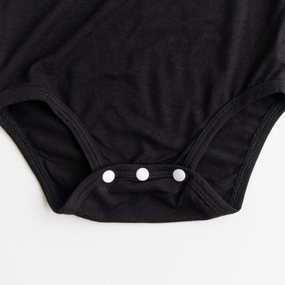 
A close-up detail shot of the three-snap closure on the bottom of the Apostle Living Inc. Faith and Freedom baby onesie in black, showing the three white snaps.
