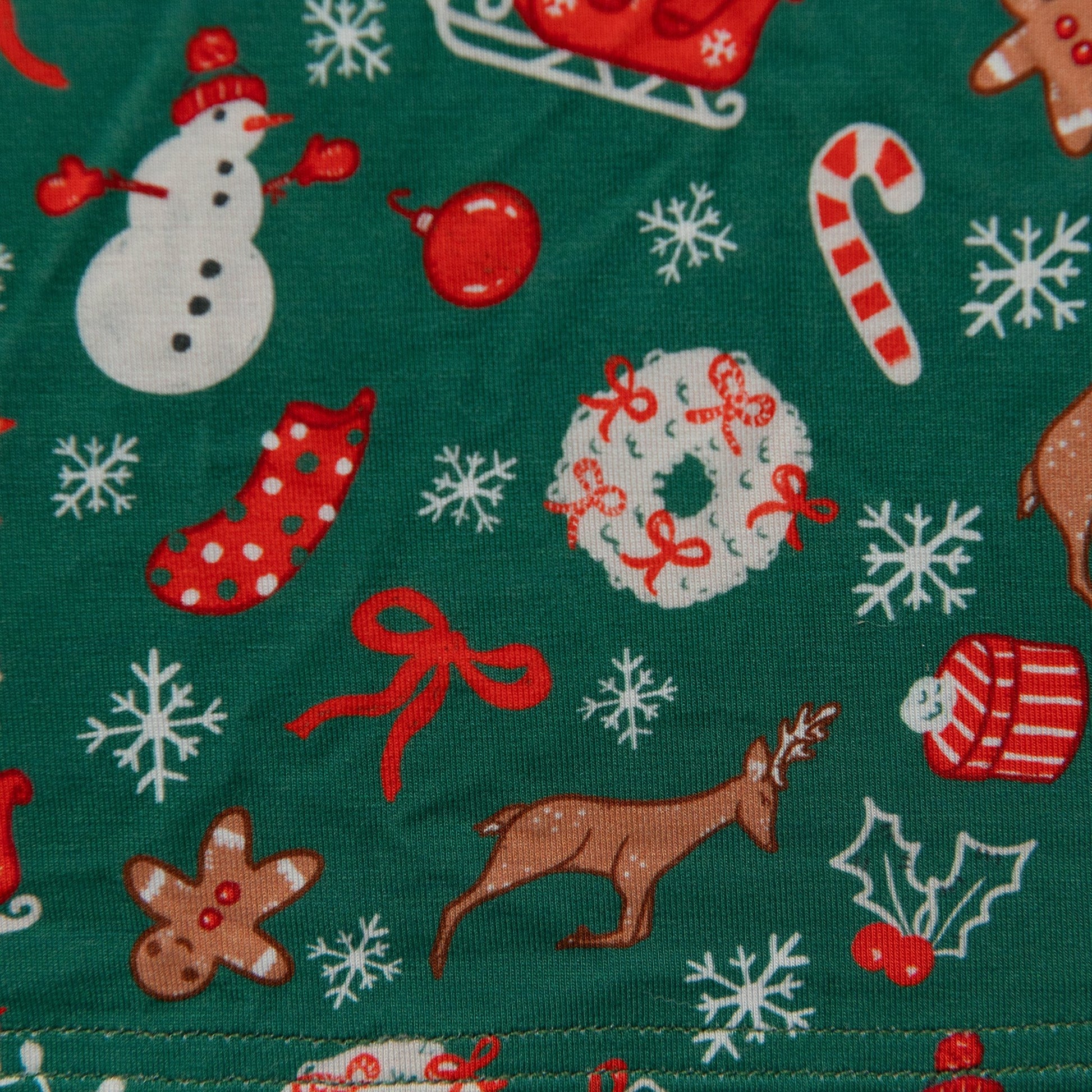 A close-up of a green infant onesie in a soft bamboo fabric, showing the detailed festive print with snowmen, reindeer, and candy canes.
