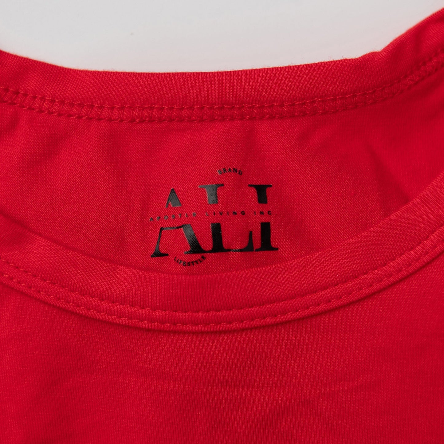 A close-up detail shot of the black Apostle Living Inc. brand tag on the collar of a red men's Christmas pajama shirt.