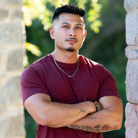 A man wearing a maroon lyocell tee, with his arms crossed in an outdoor setting.
