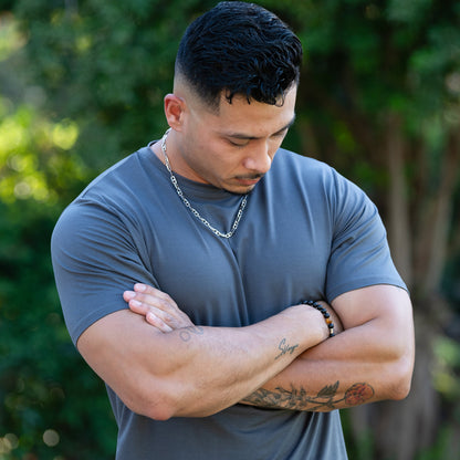 A man modeling a gray lyocell tee, with his arms crossed and looking down in a close-up outdoor shot.